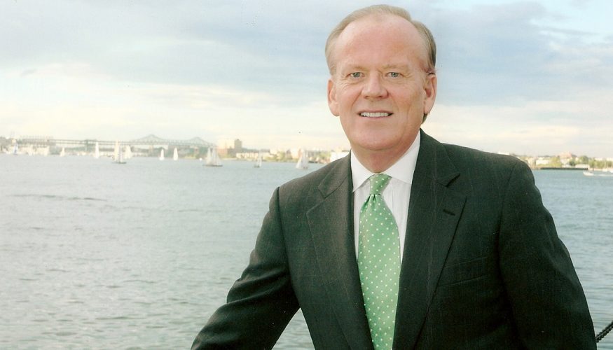 Jim Brett in a suit with the ocean and a city in the background