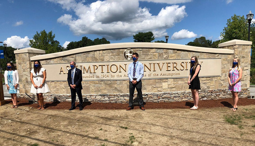 Assumption University exterior sign with individuals standing in front of it with masks on