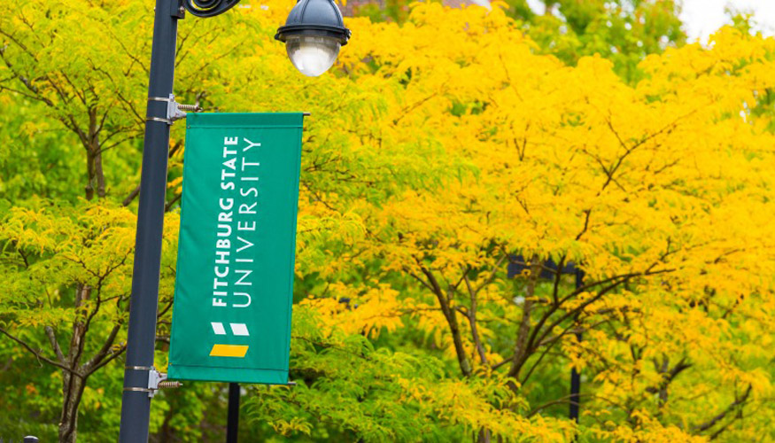 Fitchburg State banner on lamp post with tree in background