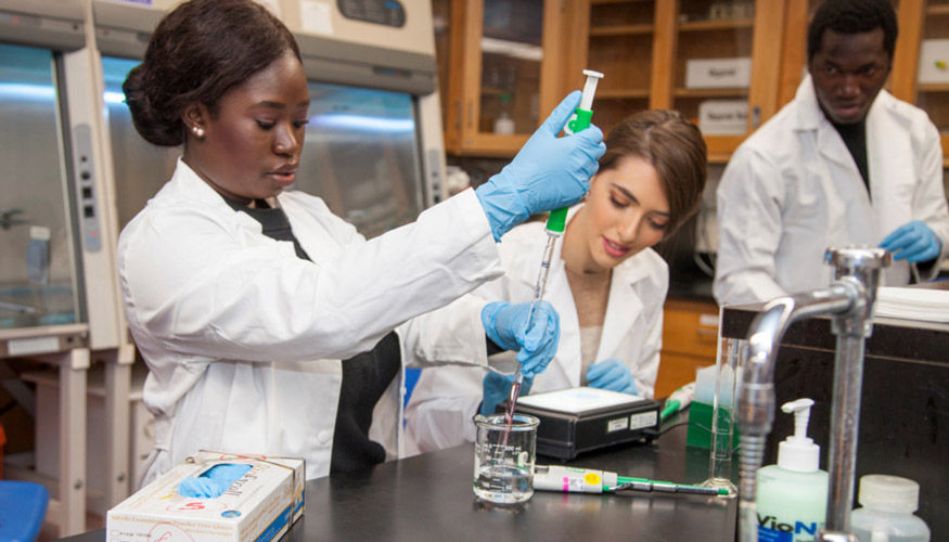 lab students in lab with coats on, doing an experiment