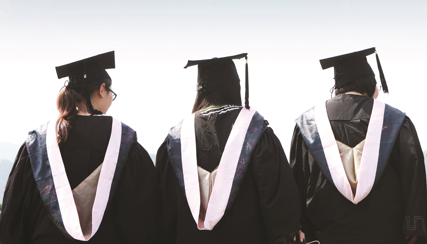 three students in graduation caps and gowns facing away from the camera