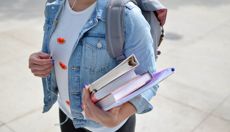 a student in a jean jacket holding some books