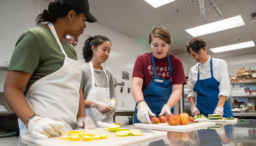 Three students prepping fruit and vegetables with a lunch lady